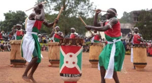 Traditional dancers from Burundi jointly beat a drum as their fellow dancers beat their own drums in the background