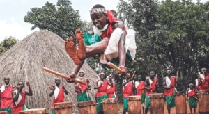 A traditional dancer from Burundi jumps up in the air as his fellow dancers beat drums in the background