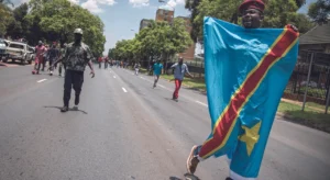 A protester in the streets carries the DRC flag with other protesters following behind