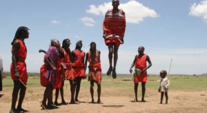 Kenyan maasai men and a child watch as one of them jumps high up in the air