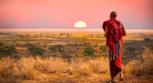 A Tanzanian Maasai man walking towards the sunset in the Savanna grasslands of the Great Lakes region.