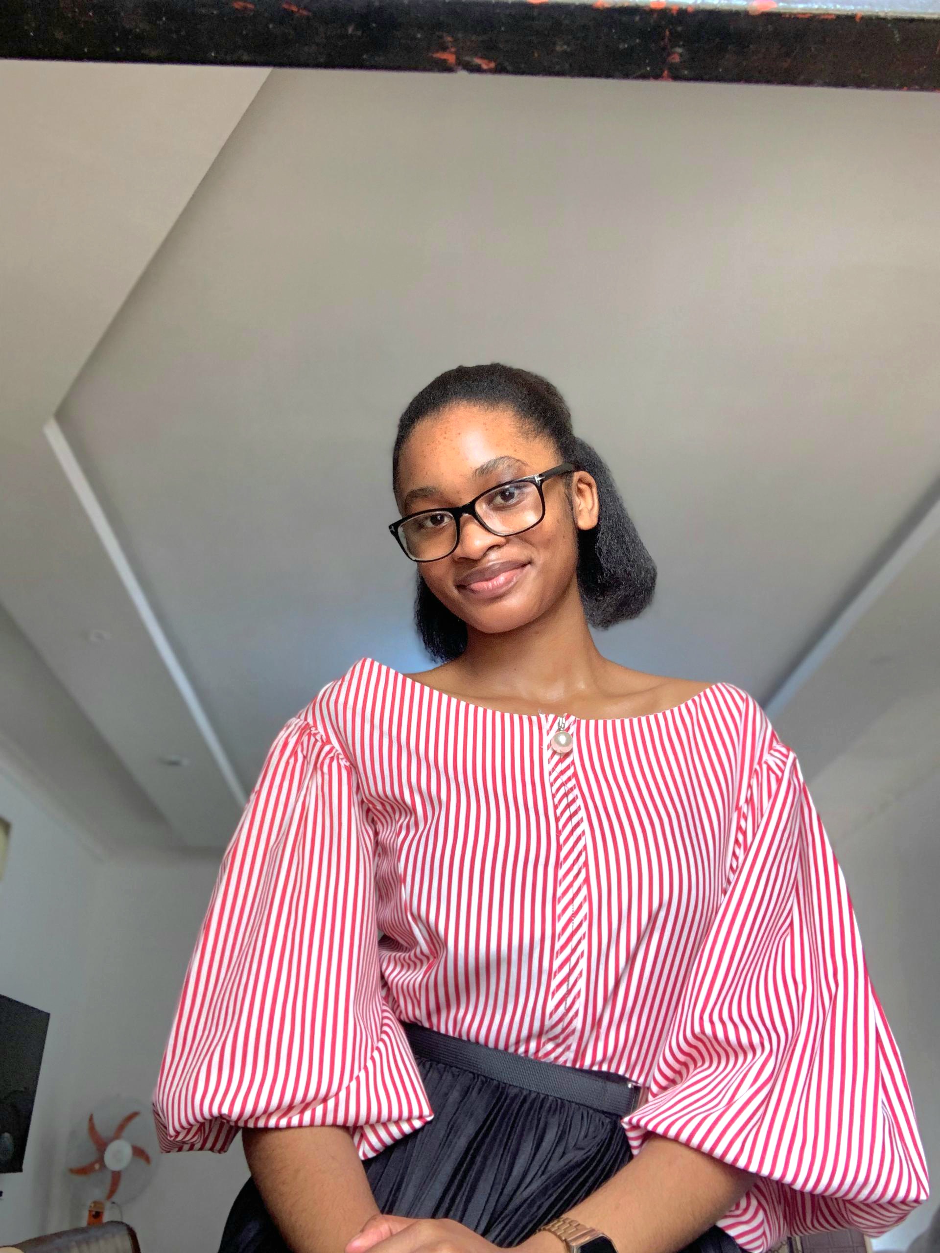 Linda Birindwa smiling, looking lovely in a pink blouse and black pants in a room